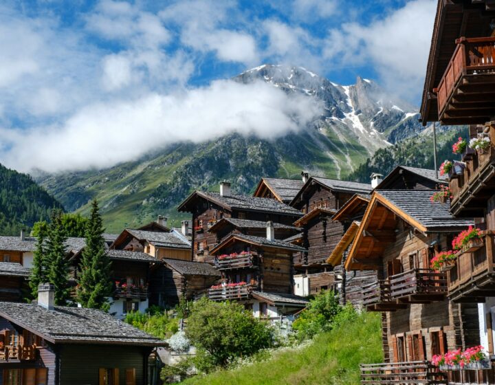 brown wooden houses near green trees and mountain under white clouds during daytime